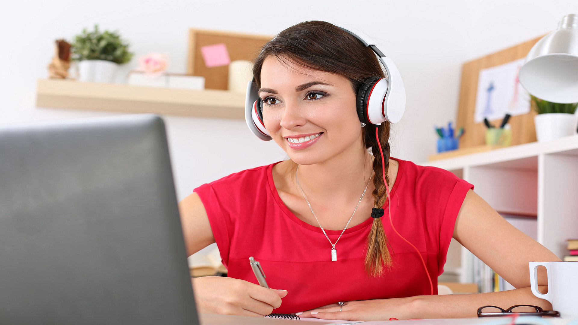 Woman in a red top wearing headphones, learning at her computer