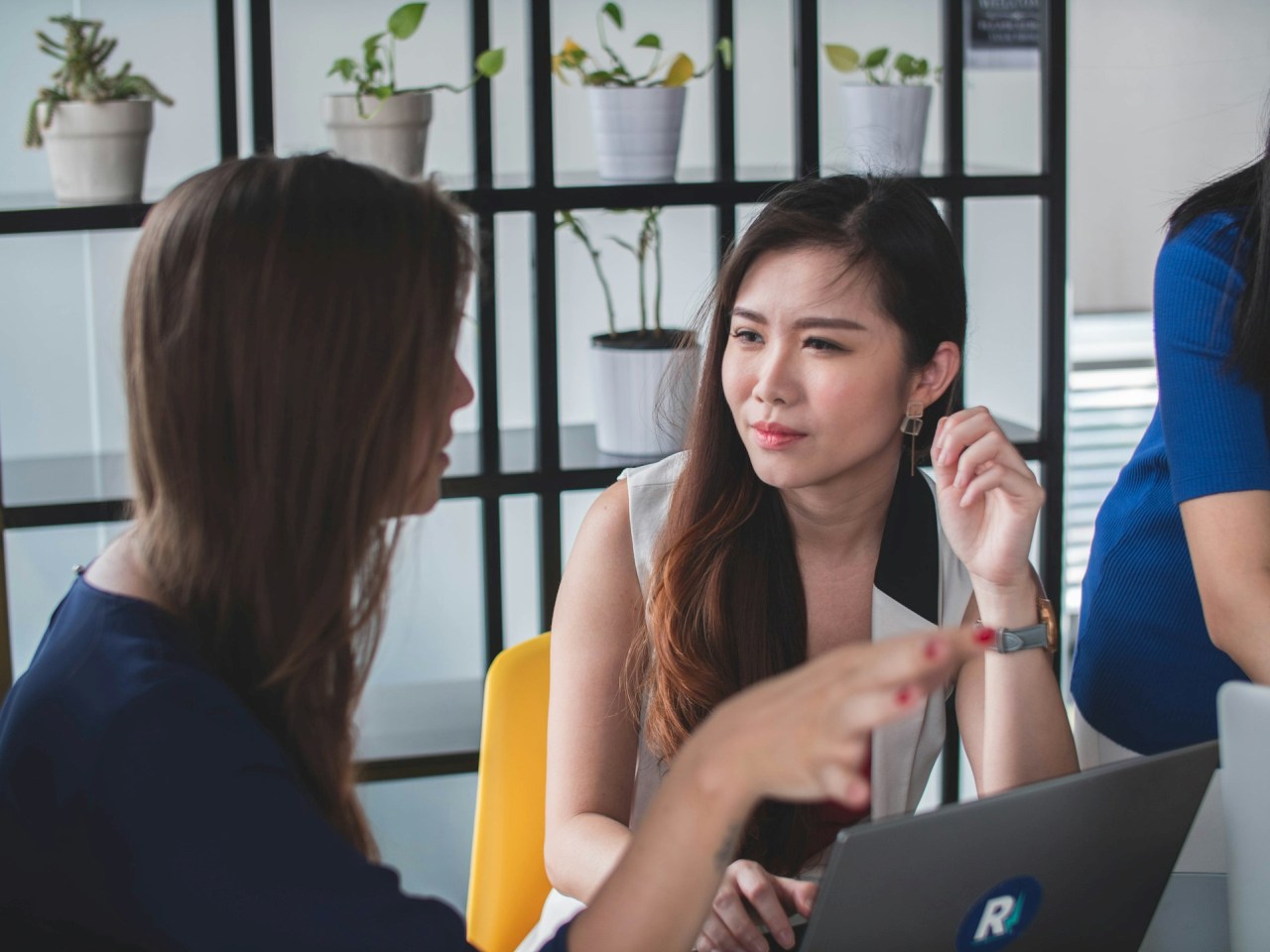 Two women talking together at work beside a laptop