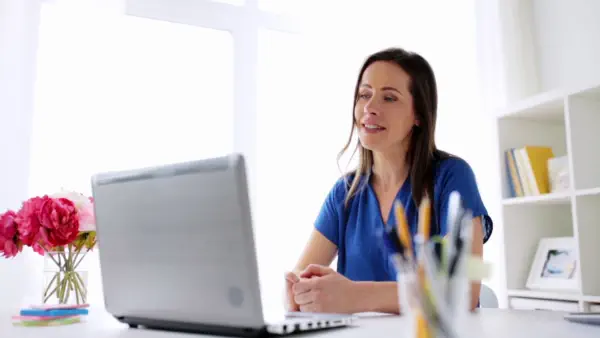 A woman wearing a blue shirt learning English online at her laptop
